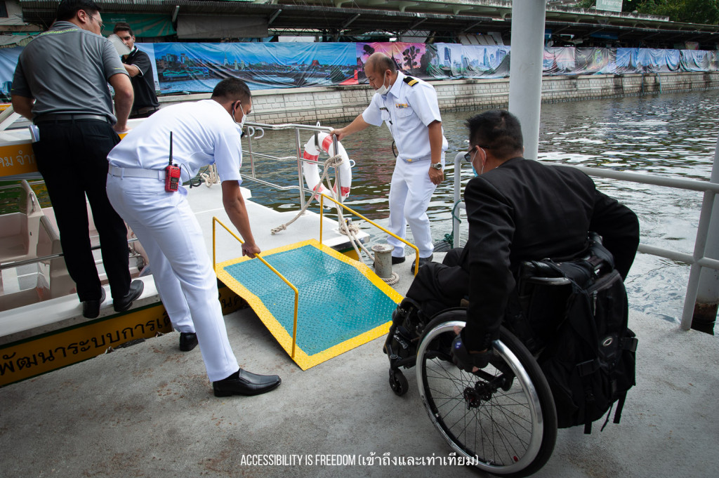 ภาพ พี่ซาบะกำลังเข็นรถขึ้นทางลาด ขึ้นเรือ มี จนท ใส่ชุดขาวกำลังคอยให้บริการ