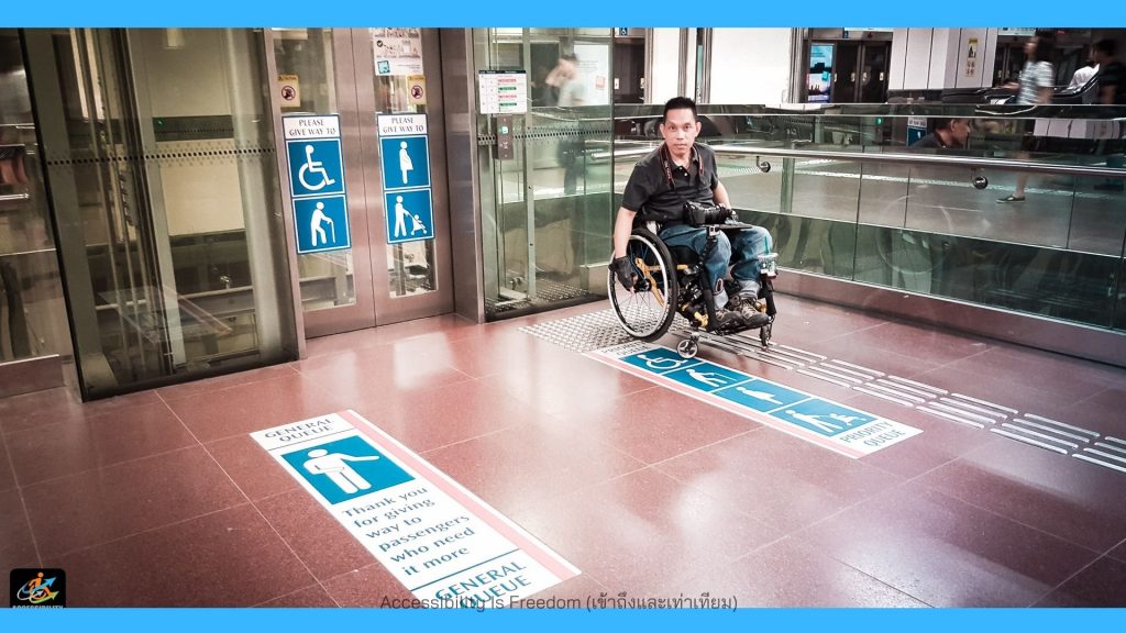 ภาพ พี่ซาบะกำลังชี้สัญลักษณ์ priority que ที่พื้นหน้าลิฟท์